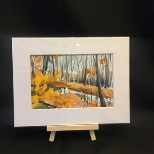 May include: A framed painting of a forest scene with a stream running through it. The trees are mostly bare, but some have yellow leaves. The stream is a light blue color and reflects the sky. The painting is on a small easel.