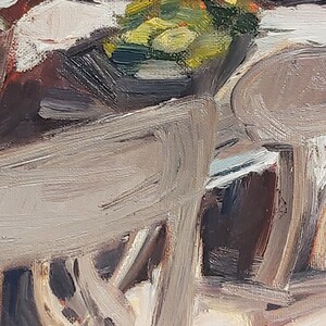 May include: A close-up of a wooden chair with a light brown finish. The chair is partially obscured by a bowl of green and yellow fruit.