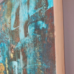 May include: Abstract painting on canvas with a blue, green, and gold color scheme. The painting has a textured surface and is framed in a natural wood frame.