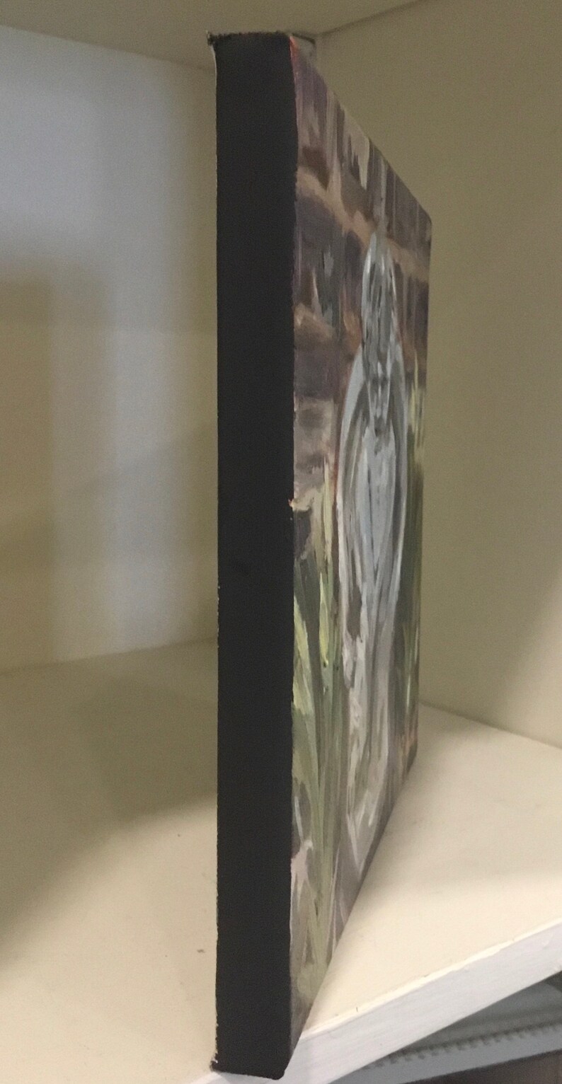 May include: A painting of a white statue of an angel with wings, standing in a garden setting. The angel is painted in a realistic style with details of the wings and the folds of the gown. The background is a blurred impression of a brick wall and green foliage.