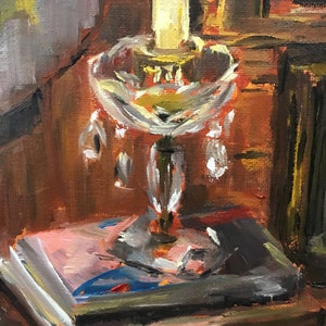 May include: A vintage-style lamp with a clear glass shade and crystal accents sits on a wooden table with a stack of books. The lamp is lit, casting a warm glow on the scene.