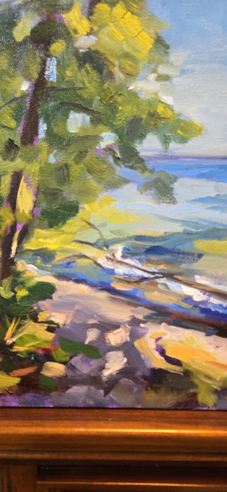May include: A painting of a tree with green leaves and a yellow trunk, overlooking a blue body of water. The foreground is a rocky, purple and brown landscape.