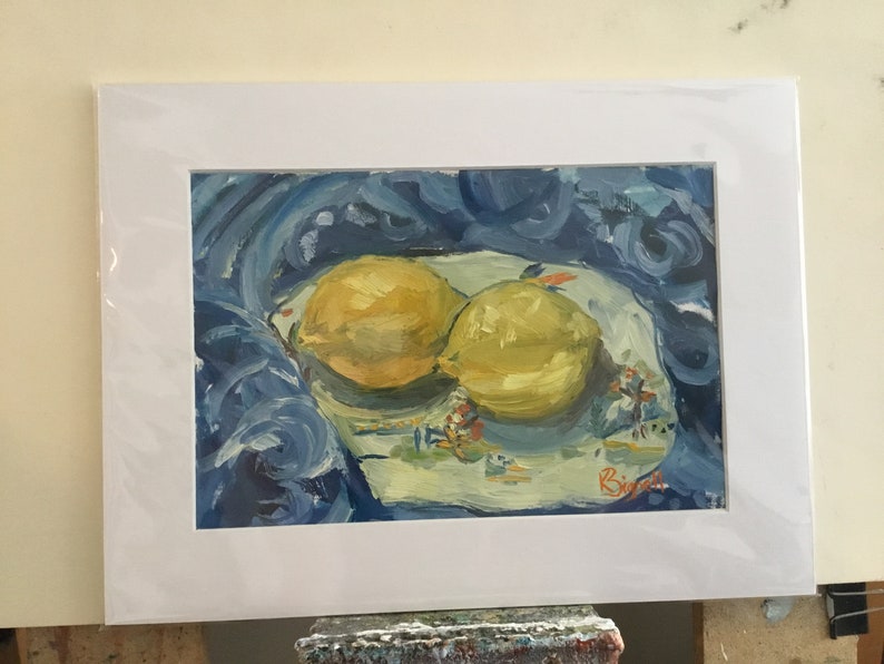 May include: A painting of two yellow lemons on a white plate with blue and white floral designs. The plate is on a blue cloth with swirling brushstrokes. The artist's signature is in the bottom right corner.