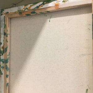 Op de afbeelding: Close-up van de achterkant van een opgespannen canvas schilderij. Het canvas is wit en het houten frame is bevlekt met groene en gele verf.