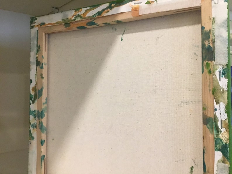 Op de afbeelding: Close-up van de achterkant van een opgespannen canvas schilderij. Het canvas is wit en het houten frame is bevlekt met groene en gele verf.