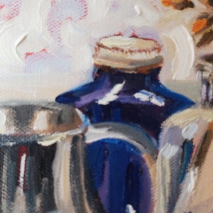 May include: A close-up of a blue glass bottle with a white lid. The bottle is partially obscured by a silver object. The background is a blurry white and orange.