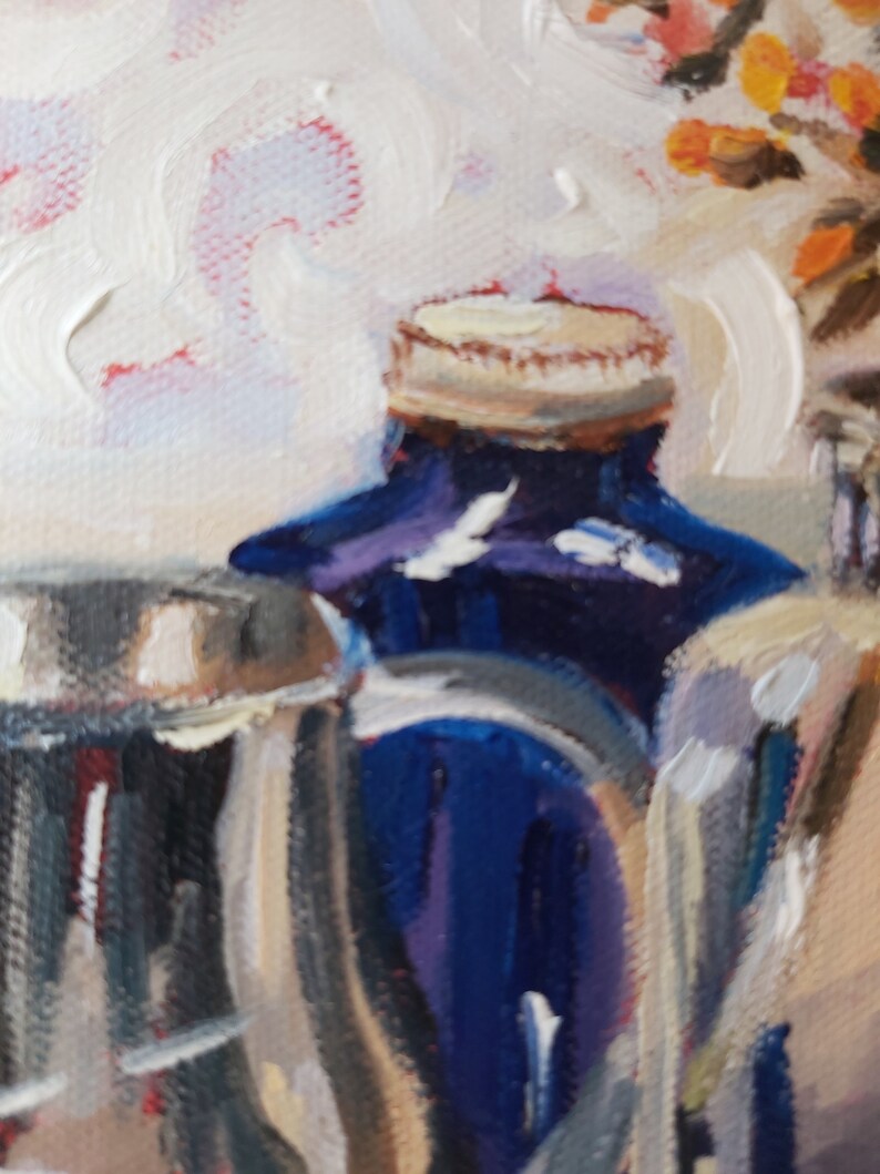 May include: A close-up of a blue glass bottle with a white lid. The bottle is partially obscured by a silver object. The background is a blurry white and orange.