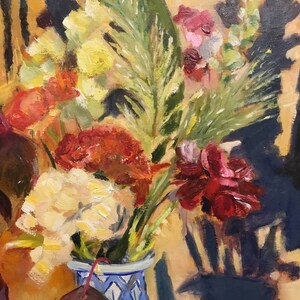 May include: A bouquet of flowers in shades of red, yellow, and green, arranged in a blue and white ceramic vase with a floral pattern. The vase is sitting on a table with a yellow background.