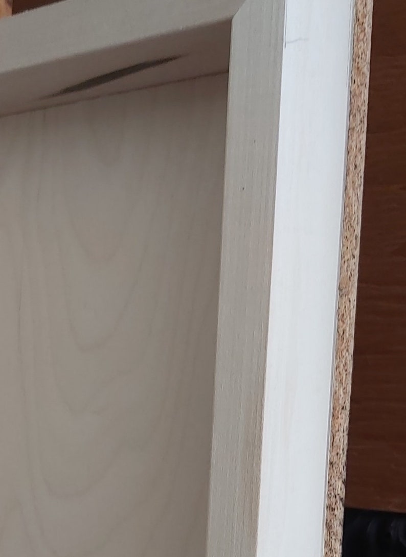 May include: Close-up of a wooden frame with a light-colored interior and a light-colored exterior edge. The frame appears to be unfinished, with visible wood grain. The side of the frame is made of a composite material.