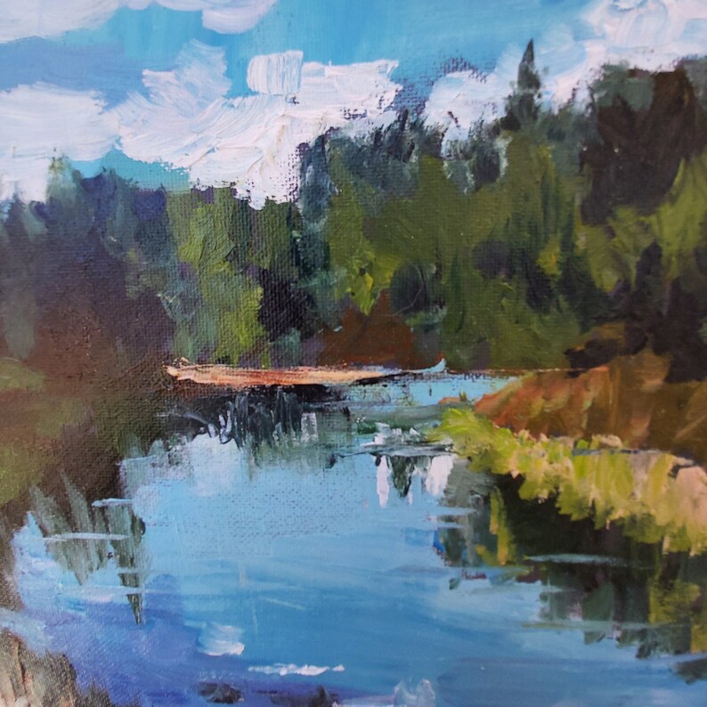 Puede incluir: Una pintura que representa una escena de bosque con un lago azul en primer plano. Los &aacute;rboles son una mezcla de verde y marr&oacute;n, y el cielo es azul claro con nubes blancas. El lago refleja el cielo y los &aacute;rboles.