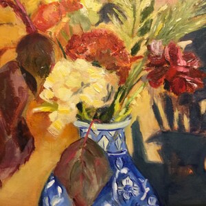 May include: A blue and white porcelain vase with a floral design holds a bouquet of yellow, red, and white flowers. A single brown leaf is tucked behind the vase.