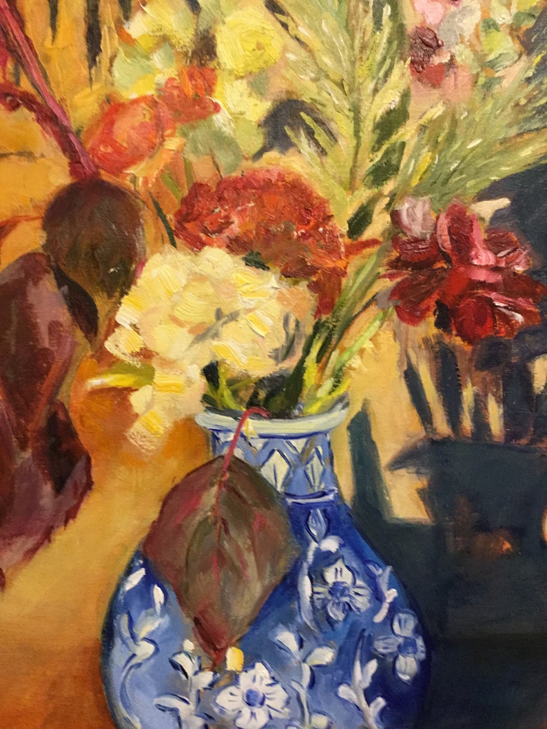 May include: A blue and white porcelain vase with a floral design holds a bouquet of yellow, red, and white flowers. A single brown leaf is tucked behind the vase.