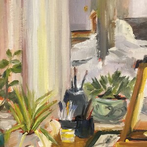 Puede incluir: Una pintura al &oacute;leo que representa una naturaleza muerta. Una planta en maceta con largas hojas verdes en una maceta blanca y beige. Pinceles y l&aacute;pices est&aacute;n en recipientes negros. Tambi&eacute;n se ve una peque&ntilde;a planta verde en maceta.