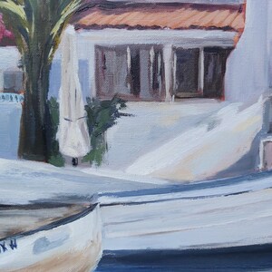 May include: Two white wooden boats with a blue stripe on the bottom. The boat in the foreground has the text "LYNX W" on the side. The boats are docked in front of a white building with a red tile roof.