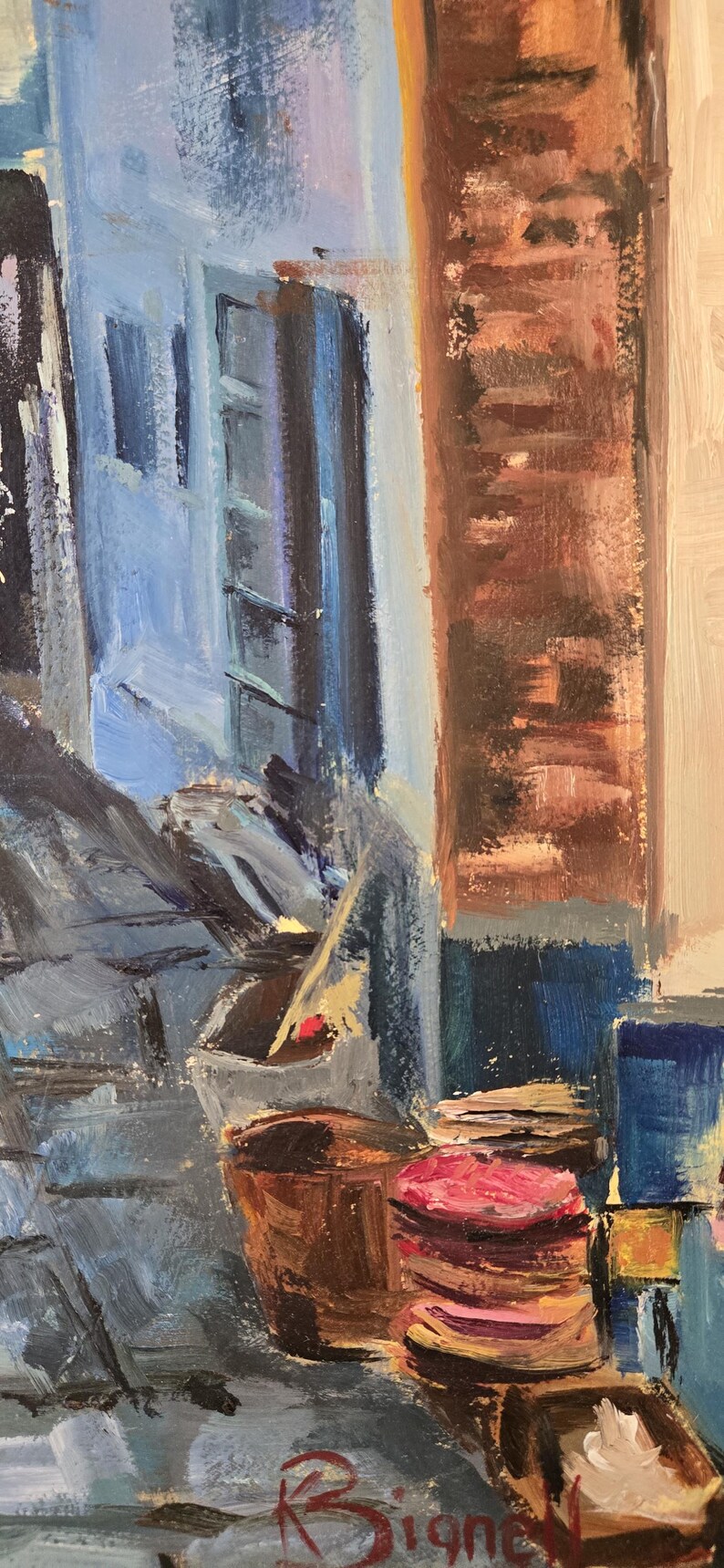 May include: Oil painting of a European street scene with blue buildings, brown barrels, and a red and pink stack of items. The artwork has visible brushstrokes and a signature in the bottom right corner.