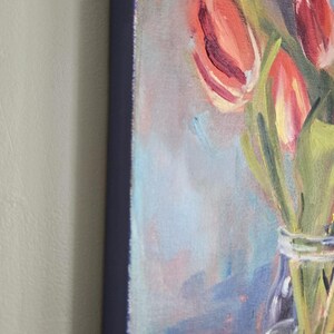 Puede incluir: Pintura al &oacute;leo de tulipanes en un jarr&oacute;n de cristal. La obra presenta tulipanes rojos y amarillos con tallos y hojas verdes. El fondo tiene suaves tonos azules y morados, y el lienzo tiene un borde azul oscuro.