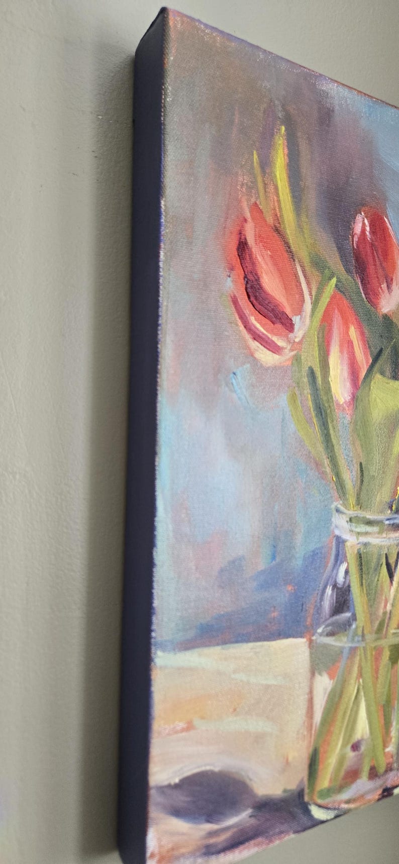 Puede incluir: Pintura al &oacute;leo de tulipanes en un jarr&oacute;n de cristal. La obra presenta tulipanes rojos y amarillos con tallos y hojas verdes. El fondo tiene suaves tonos azules y morados, y el lienzo tiene un borde azul oscuro.