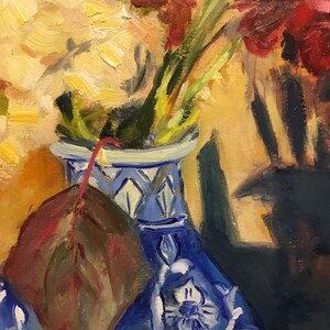 May include: A blue and white porcelain vase with a floral pattern, filled with red and yellow flowers. A single brown leaf is resting on the vase.
