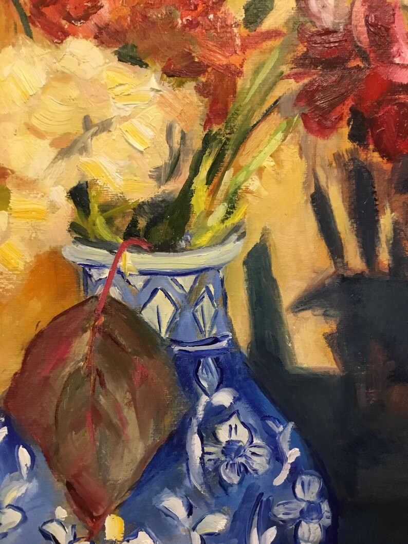 May include: A blue and white porcelain vase with a floral pattern, filled with red and yellow flowers. A single brown leaf is resting on the vase.