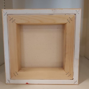 May include: The back of a wooden canvas frame with staples holding the canvas in place.
