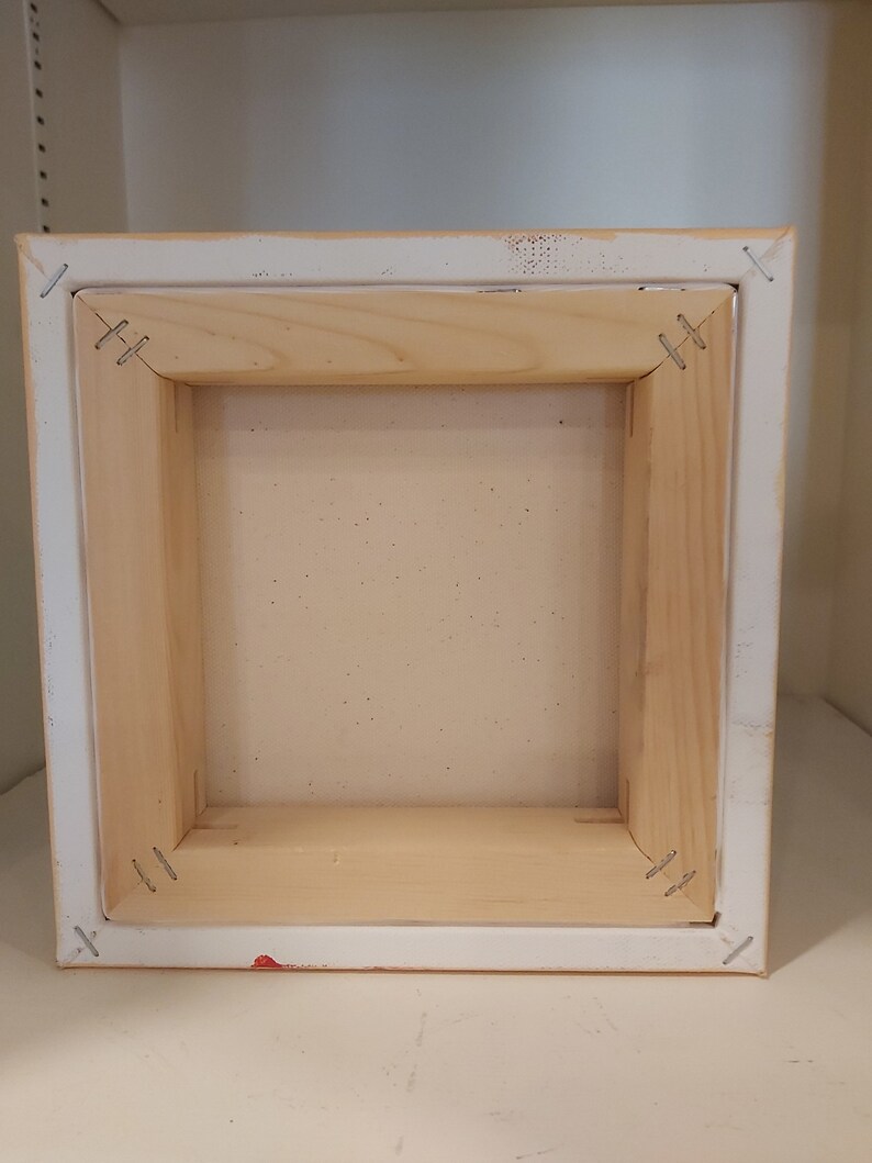 May include: The back of a wooden canvas frame with staples holding the canvas in place.