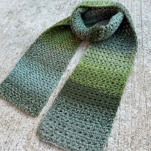 May include: A green and gray ombre crochet scarf with a textured stitch pattern.
