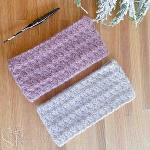 May include: Two crocheted headbands, one in a light purple colour and the other in a light grey colour. Both headbands have a textured, raised stitch pattern.