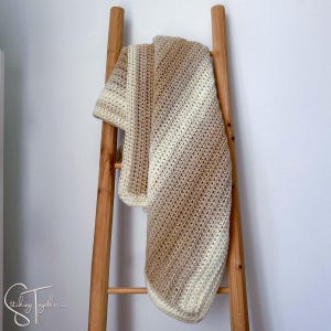 May include: A beige and white crocheted throw blanket draped over a wooden ladder. The blanket has a diagonal stripe pattern.