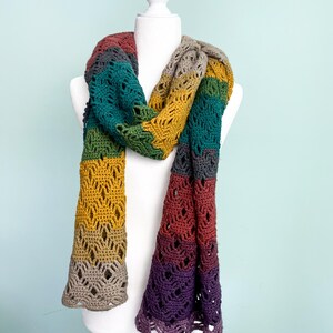 Puede incluir: Una bufanda de ganchillo multicolor con un patr&oacute;n de encaje. La bufanda est&aacute; hecha en tonos de morado, rojo, naranja, amarillo, verde y gris.