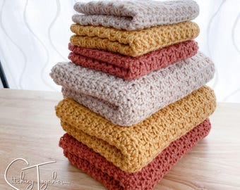 Puede incluir: Una pila de seis paños de cocina de ganchillo en varios colores: beige, amarillo mostaza y terracota. Los paños están cuidadosamente doblados y apilados uno encima del otro. La imagen está tomada desde un ángulo ligeramente elevado.