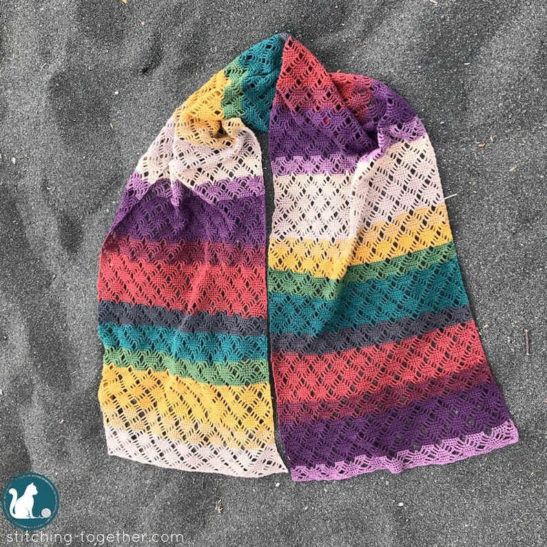 Puede incluir: Una bufanda de crochet colorida con un patr&oacute;n de encaje. La bufanda est&aacute; hecha con una variedad de colores, incluyendo morado, rojo, amarillo, verde y azul.