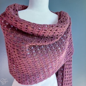 May include: A hand-crocheted shawl in variegated shades of dusty rose, mauve, and deep plum. The textile features an open, repeating geometric stitch pattern that creates a lightweight, airy texture throughout the entire length of the garment.