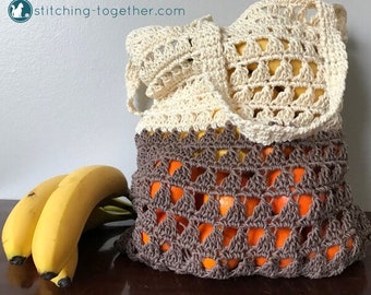 May include: A crocheted produce bag with a cream top and brown bottom. The bag is filled with oranges and is sitting on a wooden surface next to a bunch of bananas.