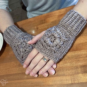 May include: A pair of crocheted fingerless gloves with a floral design. The gloves are a light brown color and have a textured pattern.