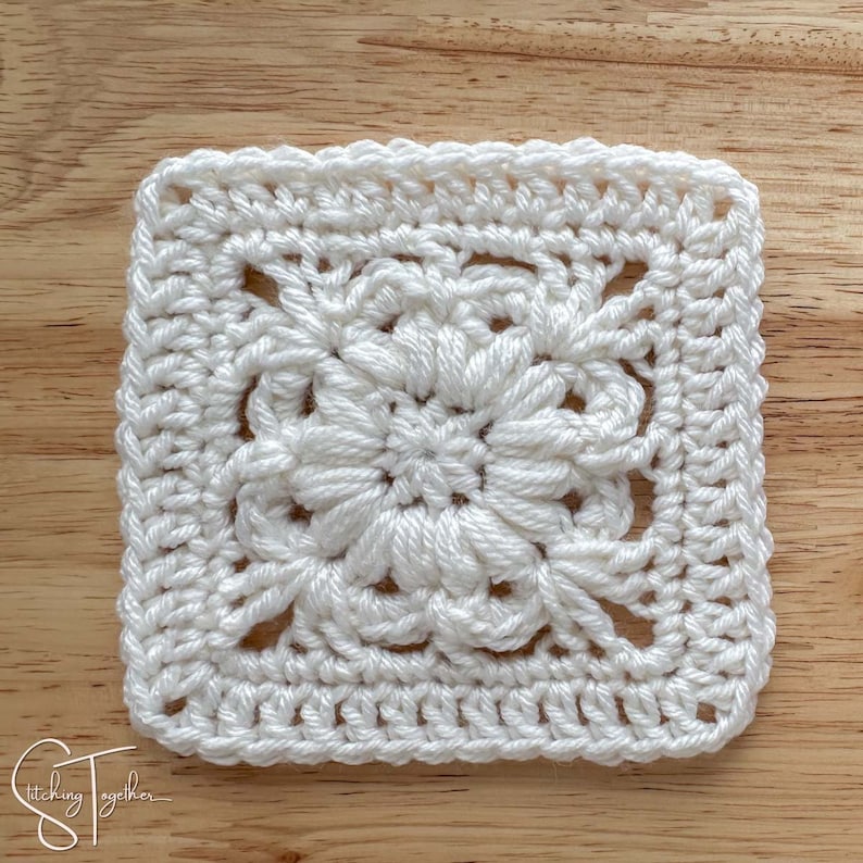 May include: A white crochet square with a detailed floral design in the center. The square is made with a single crochet stitch and has a border around the edge.