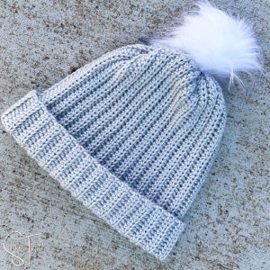 May include: A gray crocheted beanie with a white faux fur pom pom on top.