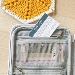 May include: A gray crochet hook case with a zipper closure. The case has multiple compartments and a mesh pocket. A crochet hook size chart is partially visible in the case. The chart lists hook sizes in millimeters and US sizes.