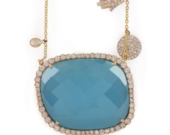 Può includere: Una collana d'oro con un grande ciondolo di pietra preziosa blu chiaro circondato da un'aureola di piccoli diamanti. La collana presenta anche un piccolo ciondolo di diamante a forma di mano e un ciondolo rotondo di diamante.