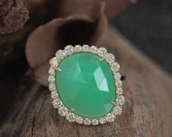 Pode incluir: Um anel de ouro com uma pedra preciosa verde e um halo de diamantes. O anel é engastado em ouro e apresenta uma grande pedra preciosa verde facetada.