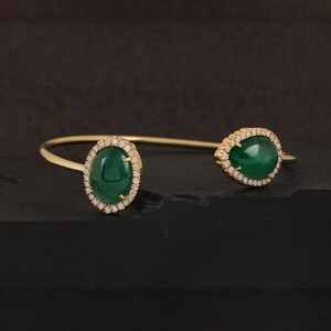 May include: A gold bangle bracelet with two oval-shaped green gemstones set in a halo of sparkling diamonds.