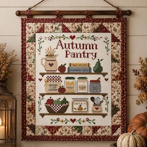 May include: A rectangular wall hanging featuring a cross-stitch design titled Autumn Pantry. The embroidery depicts shelves with jars labeled Flour, Honey, Sugar, and Pumpkin Pie, plus books and fruit. It is framed by a floral quilted border.