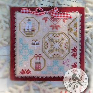May include: A framed cross-stitch sampler titled "Quaker Snippets No. 2" by Brenda Gervais. The sampler features festive winter designs in red, gold, and blue, including snowflakes and gift motifs. A red and white checkered bow adorns the top.