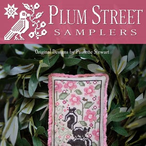 May include: A cross-stitch sampler featuring a pink and green floral design with three black and white skunks. The sampler is framed with a pink border and is titled "Stench Stack".