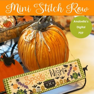 Puede incluir: Un proyecto de punto de cruz con las palabras "Spooky Night" e imágenes temáticas de Halloween. El proyecto se muestra en un soporte de metal negro, con una gran calabaza naranja en el fondo. El texto "Mini Stitch Row" está en la parte superior.
