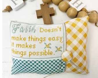 Può includere: Modello di punto croce per un cuscino con il testo "Faith Doesn't Make Things Easy, It Makes Things Possible." Il cuscino è a quadri verdi e bianchi con un bordo a quadri gialli e bianchi. C'è una croce di legno e una ghirlanda di perline di legno con la parola "FAITH" scritta in lettere bianche.
