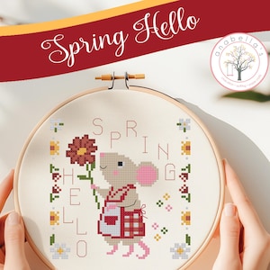 May include: Cross-stitch embroidery in a wooden hoop featuring a mouse holding a flower. The design includes the words "Spring Hello" and is surrounded by floral accents. The text "Anabella's Needleart" is also present.