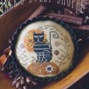 May include: A cross stitch pattern featuring a black cat sitting on a pie crust with a moon and stars in the background. The pattern is titled "Olga's Tart" and is part of the "Plum Street Samplers" collection.