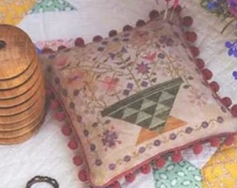 Può includere: Un cuscino in tessuto stampato con un motivo a cestino floreale e bordatura con pompon rossi è appoggiato su una trapunta patchwork. Una bobina di legno e forbici vintage sono accanto al cuscino. L'immagine include il testo "Pansy Patch Quilts and Stitchery" e "Betsy's Summer Basket".