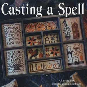 May include: A cross stitch pattern book titled "Casting a Spell" featuring a black and white illustration of a witch's cauldron with a cat and a raven. The book is by Blackbird Designs and includes a sewing box with two extra pincushions.