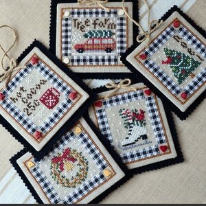May include: Five cross-stitch ornament patterns featuring winter holiday themes. The patterns are framed in black and white gingham fabric and feature designs like a Christmas tree, a wreath, a car with a Christmas tree on top, a cup of hot cocoa, and a pair of ice skates. The patterns are titled "Country Christmas I" and "NW-62".